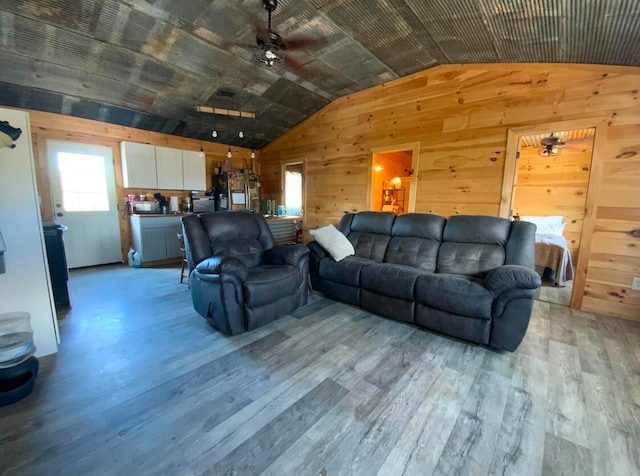 living room with light hardwood / wood-style floors, lofted ceiling, wooden walls, and ceiling fan