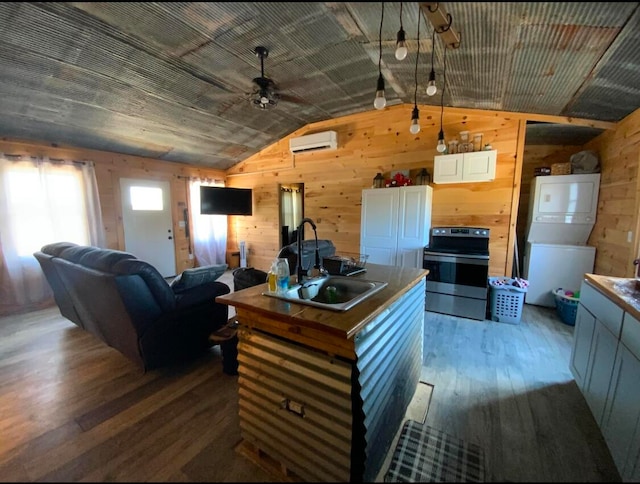 kitchen with lofted ceiling, hardwood / wood-style flooring, range with electric cooktop, sink, and stacked washer / dryer