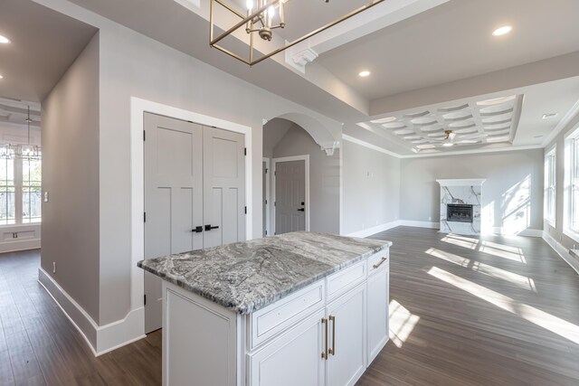 kitchen with light stone counters, dark hardwood / wood-style flooring, a premium fireplace, white cabinetry, and a center island