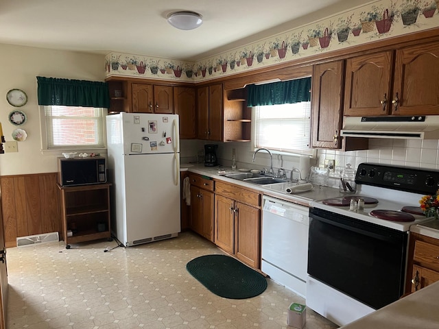 kitchen with backsplash, white appliances, sink, and wooden walls