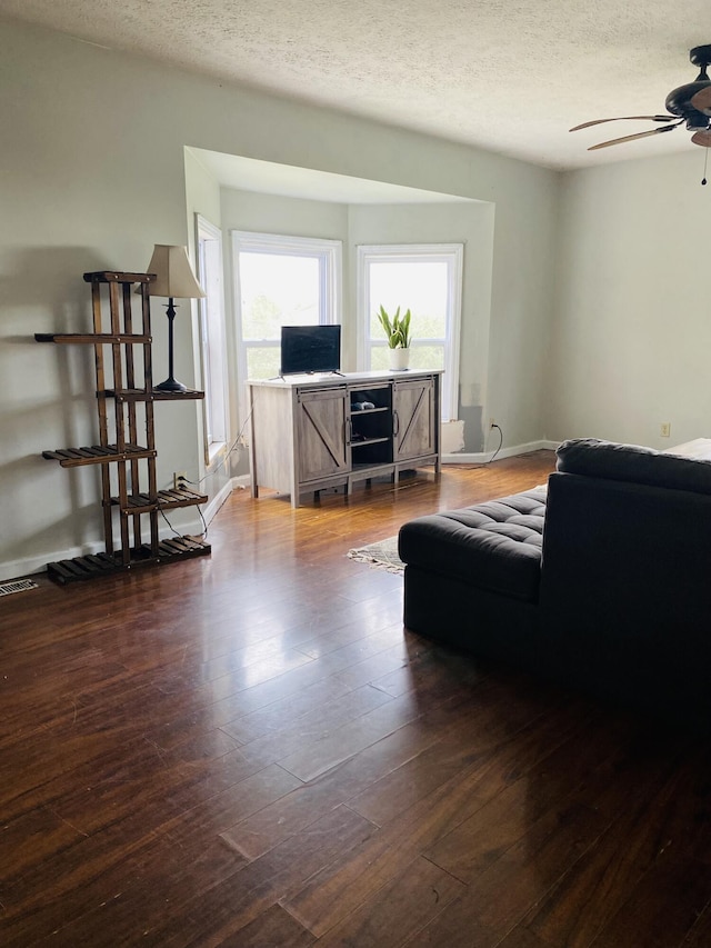 living room featuring dark hardwood / wood-style floors, ceiling fan, and a textured ceiling