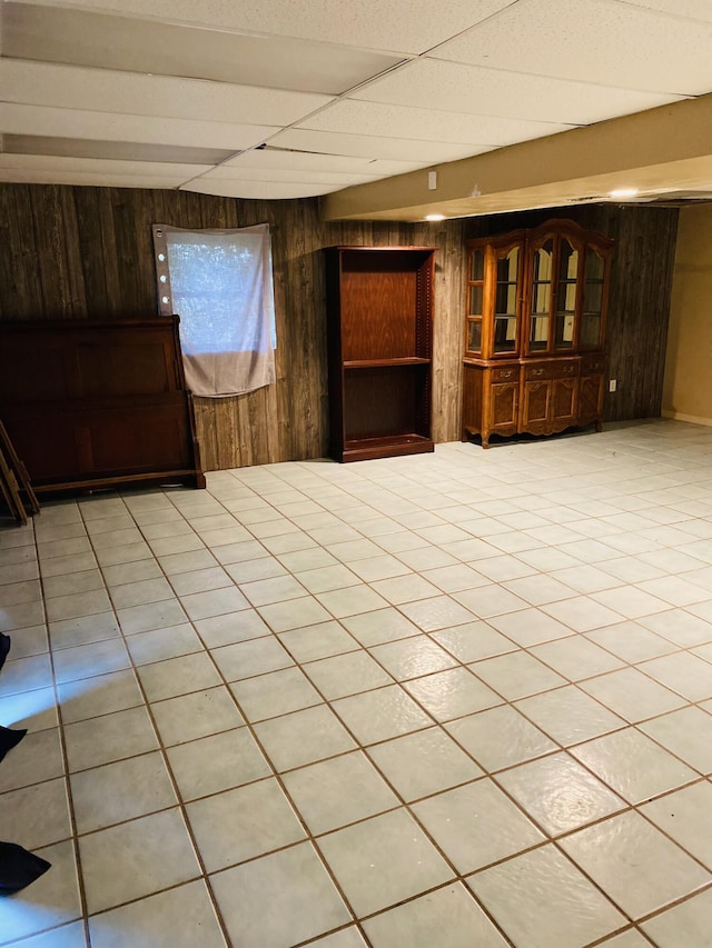 unfurnished room with light tile patterned floors, a drop ceiling, and wooden walls