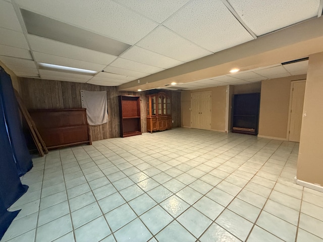 basement with a paneled ceiling, wood walls, and light tile patterned floors