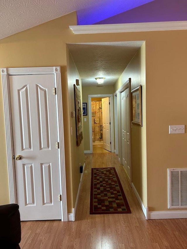 hallway featuring a textured ceiling, lofted ceiling, and light wood-type flooring