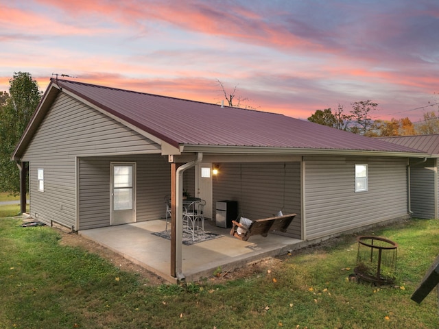 back house at dusk featuring a yard and a patio area