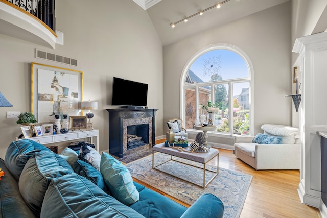 living room with a high end fireplace, track lighting, light wood-type flooring, and high vaulted ceiling