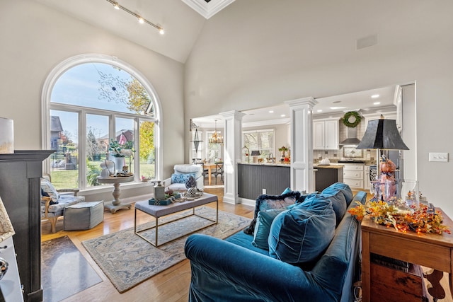 living room with ornamental molding, light wood-type flooring, high vaulted ceiling, an inviting chandelier, and decorative columns