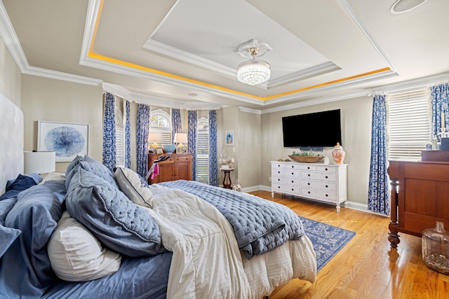 bedroom with light wood-type flooring, ornamental molding, and a raised ceiling