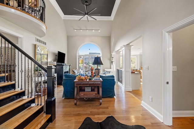 foyer entrance featuring decorative columns, rail lighting, crown molding, light hardwood / wood-style flooring, and a high ceiling