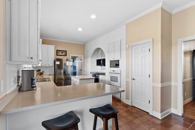 kitchen featuring stainless steel appliances, a kitchen bar, kitchen peninsula, and white cabinets