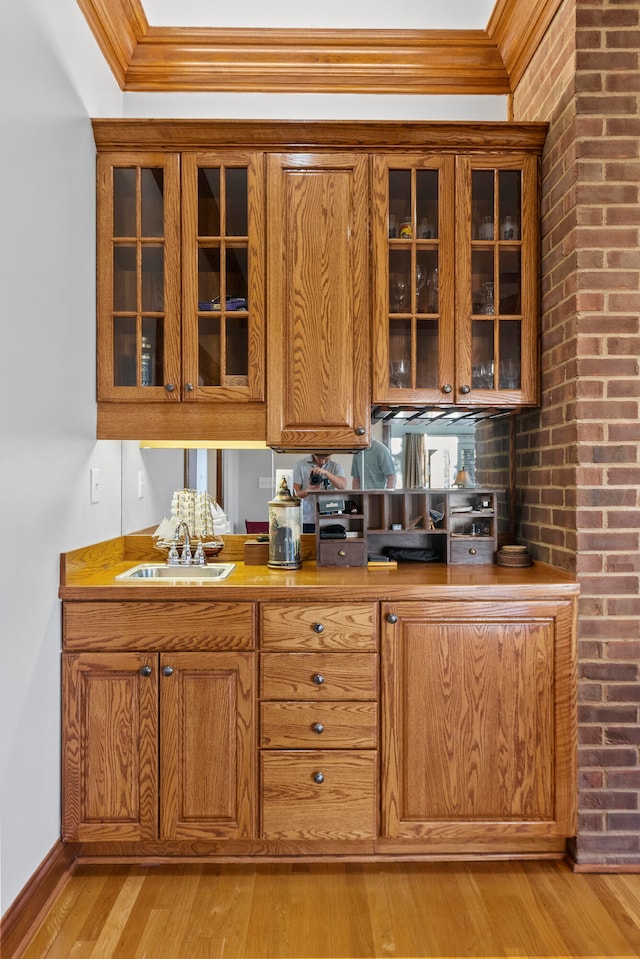 bar featuring light hardwood / wood-style floors, crown molding, sink, and brick wall