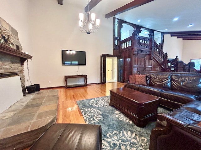 living room with beam ceiling, hardwood / wood-style floors, a towering ceiling, a fireplace, and a notable chandelier