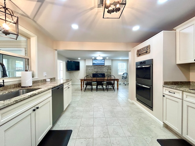 kitchen with sink, hanging light fixtures, stainless steel double oven, a stone fireplace, and black dishwasher