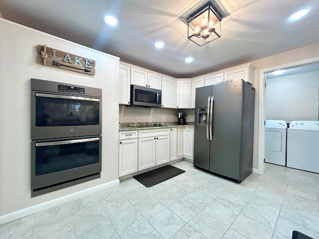 kitchen with stainless steel appliances, dark stone counters, a chandelier, white cabinetry, and washing machine and dryer