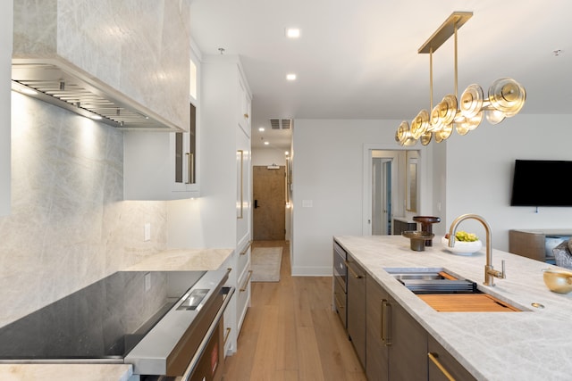 106 W Vine St Unit 407, Lexington, KY 40507 - kitchen featuring a sink, modern cabinets, light wood-style floors, wall chimney range hood, and hanging light fixtures