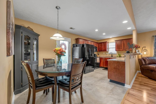 kitchen with pendant lighting, kitchen peninsula, sink, black appliances, and light hardwood / wood-style flooring