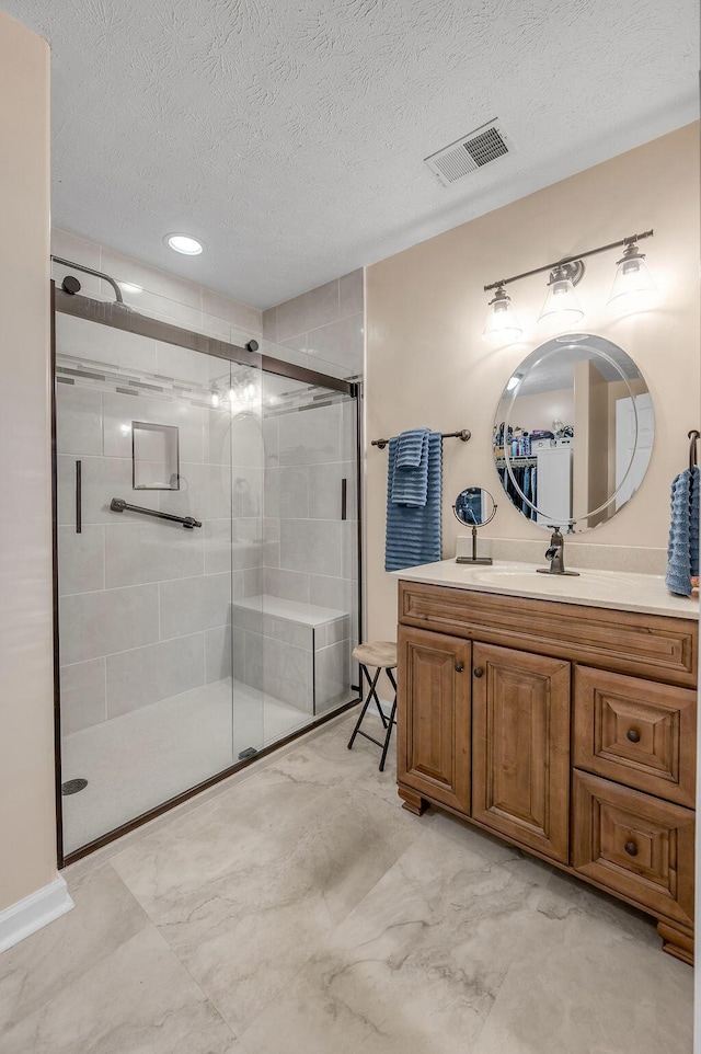 bathroom with a shower with door, vanity, and a textured ceiling