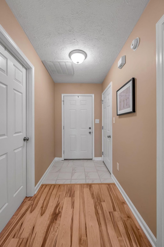 doorway to outside with a textured ceiling and light wood-type flooring