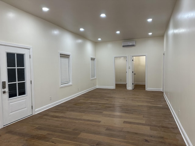 empty room with a high ceiling, a wall mounted air conditioner, and dark hardwood / wood-style floors