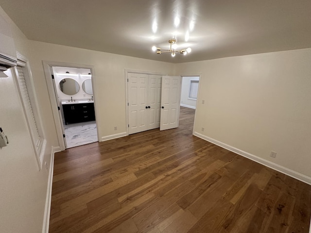 unfurnished bedroom with a closet, ensuite bath, sink, a chandelier, and dark hardwood / wood-style flooring