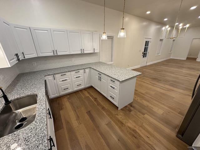 kitchen with dark hardwood / wood-style flooring, kitchen peninsula, white cabinetry, light stone counters, and decorative backsplash