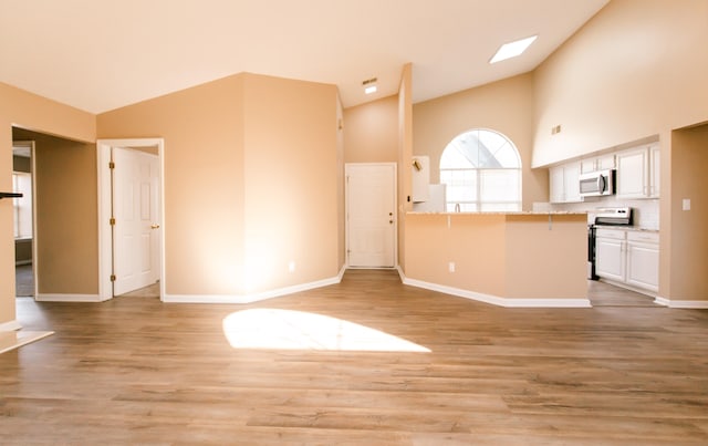 unfurnished living room featuring high vaulted ceiling, light wood-type flooring, and a skylight