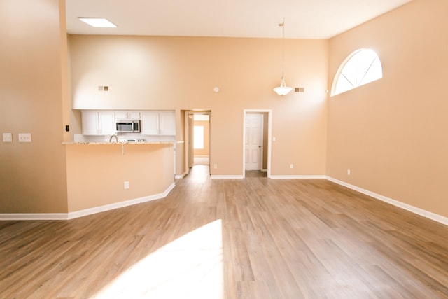 unfurnished living room with light hardwood / wood-style flooring and a towering ceiling