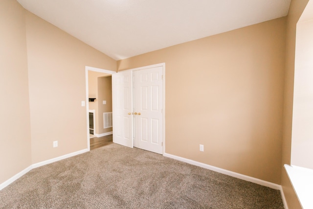 unfurnished bedroom featuring carpet flooring, vaulted ceiling, and a closet