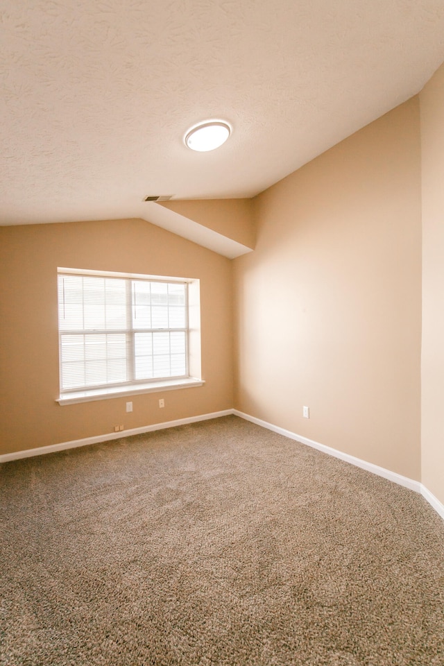 empty room with a textured ceiling, carpet flooring, and vaulted ceiling