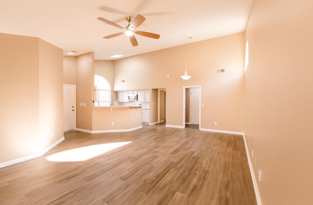 unfurnished living room featuring a high ceiling, hardwood / wood-style flooring, and ceiling fan