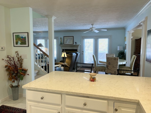 kitchen with white cabinets, ceiling fan, decorative columns, light tile patterned flooring, and crown molding