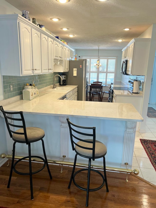 kitchen with kitchen peninsula, appliances with stainless steel finishes, white cabinetry, light hardwood / wood-style flooring, and sink