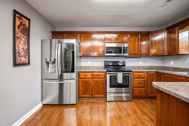 kitchen featuring a textured ceiling, stainless steel appliances, and light wood-type flooring