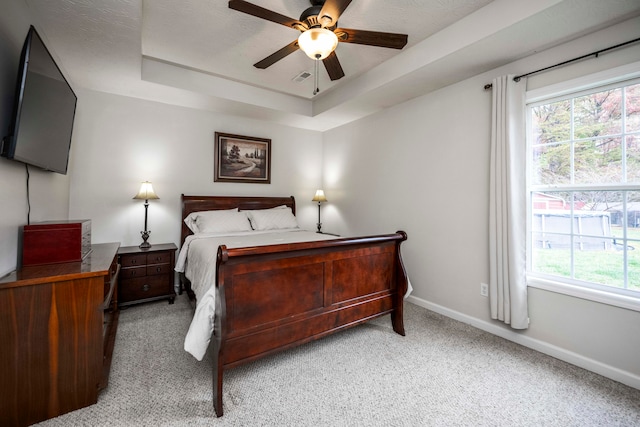 carpeted bedroom featuring a tray ceiling and ceiling fan