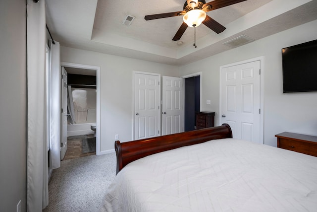 carpeted bedroom with multiple closets, ensuite bath, a raised ceiling, a textured ceiling, and ceiling fan