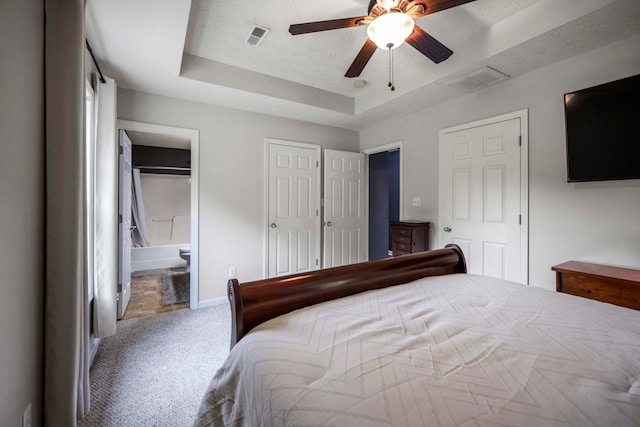 bedroom with ceiling fan, multiple closets, a tray ceiling, carpet flooring, and ensuite bath