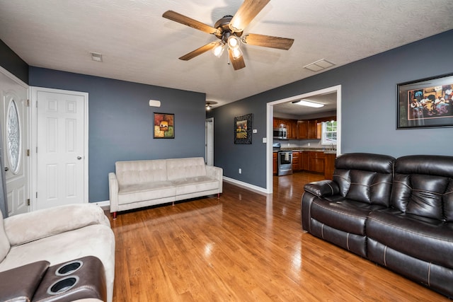 living room with a textured ceiling, sink, light wood-type flooring, and ceiling fan