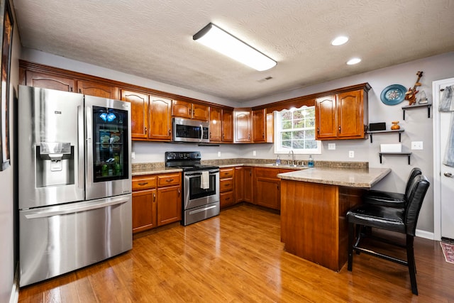 kitchen with appliances with stainless steel finishes, a textured ceiling, kitchen peninsula, a breakfast bar area, and light hardwood / wood-style flooring