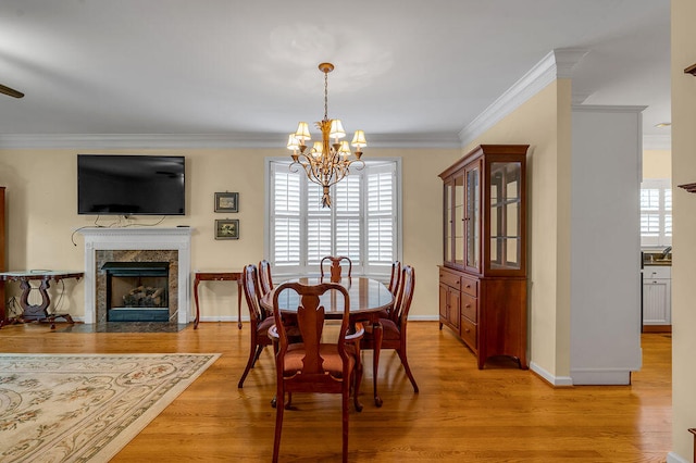 dining room featuring a premium fireplace, light wood-type flooring, an inviting chandelier, and ornamental molding