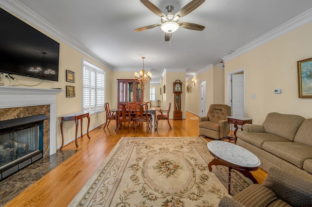 living room with ornamental molding, light wood-type flooring, ceiling fan with notable chandelier, and a premium fireplace