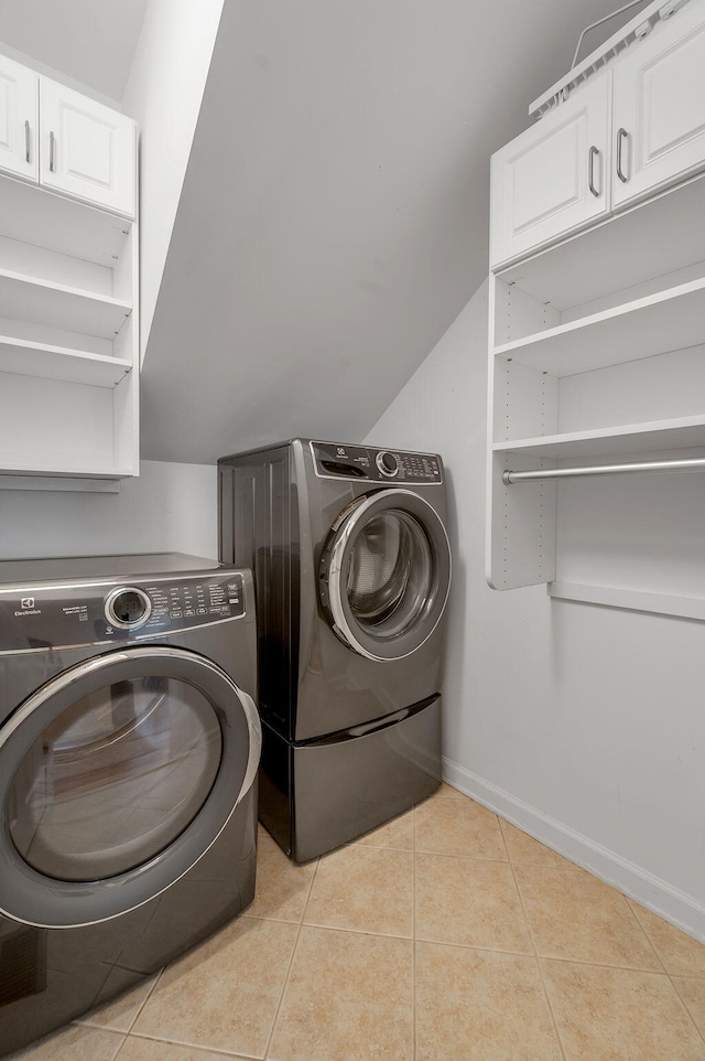 laundry area featuring washing machine and dryer, cabinets, and light tile patterned flooring