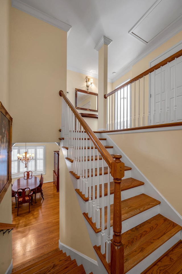 stairway with wood-type flooring, crown molding, and a notable chandelier