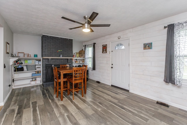 dining room with a textured ceiling, a brick fireplace, hardwood / wood-style flooring, and ceiling fan