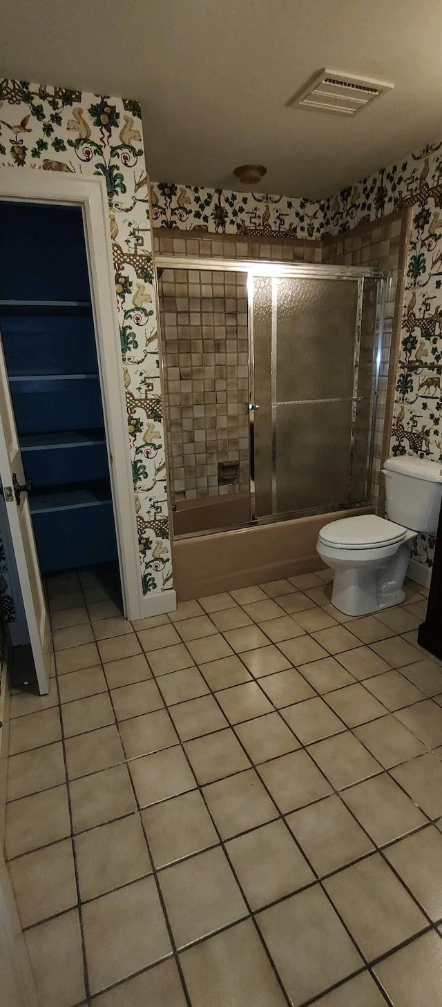 bathroom featuring tile patterned floors, toilet, and combined bath / shower with glass door