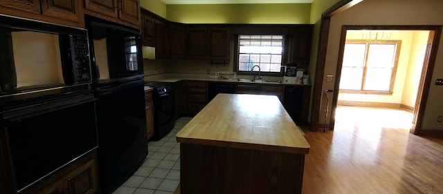 kitchen with butcher block counters, light hardwood / wood-style floors, sink, black appliances, and dark brown cabinets