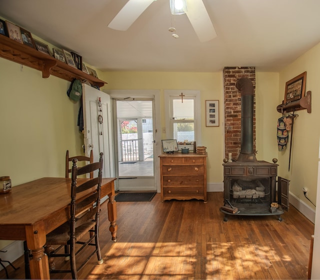 dining space featuring dark wood-type flooring, a wood stove, and ceiling fan