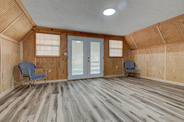 unfurnished room featuring lofted ceiling, french doors, wooden walls, light wood-type flooring, and a textured ceiling