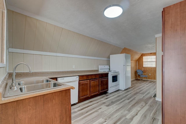 kitchen with light hardwood / wood-style flooring, sink, vaulted ceiling, white appliances, and wood walls