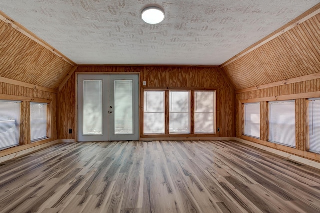 unfurnished living room featuring french doors, wood walls, wood-type flooring, and vaulted ceiling