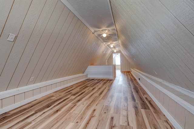 bonus room with light hardwood / wood-style flooring, ceiling fan, wooden walls, and vaulted ceiling